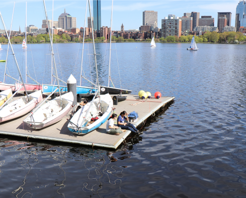 Sailboats on a dock at the MIT Sailing Pavilion with the Boston skyline in the background with the Charles River