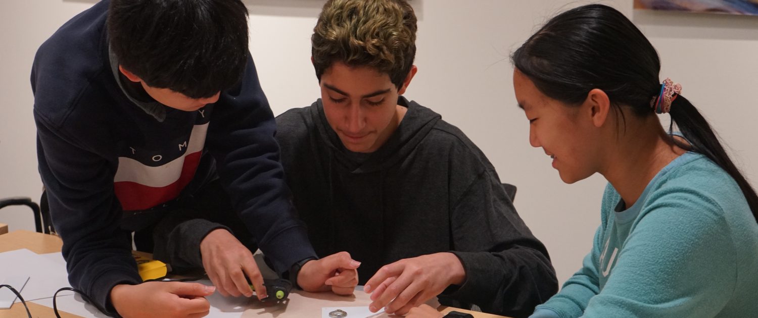 Three seated students work together on a hands-on STEM model project.