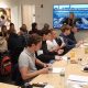 A group of students sitting for a presentation with a female speaker in front of a screen displaying a picture of the MIT campus