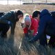 Three smiling students crouch in a salt marsh counting species of grass.