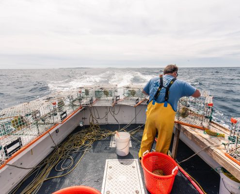 A deckhand on a lobster fishing vessel preparing equipment at sea.