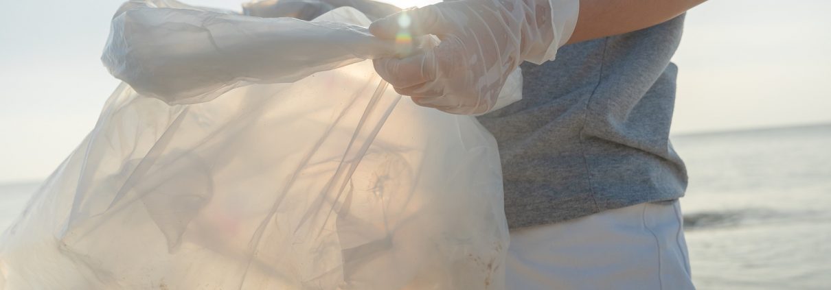 A person holds a plastic bag on the shore of a beach.