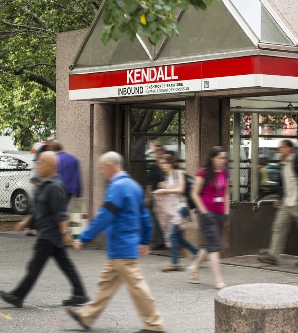 Kendall Square MBTA train station entrance with a red sign and people walking by